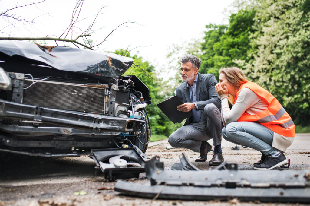 A driver and an insurance agent assess damage on a wrecked vehicle. 