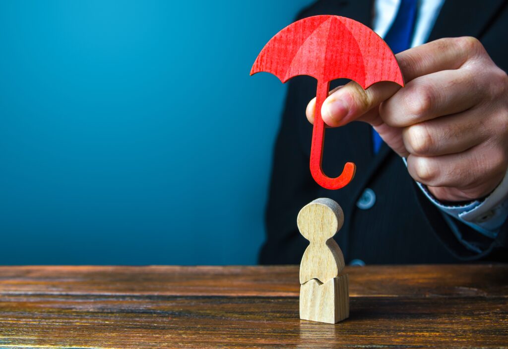 Person holding umbrella over little wooden figure to denote personal umbrella insurance