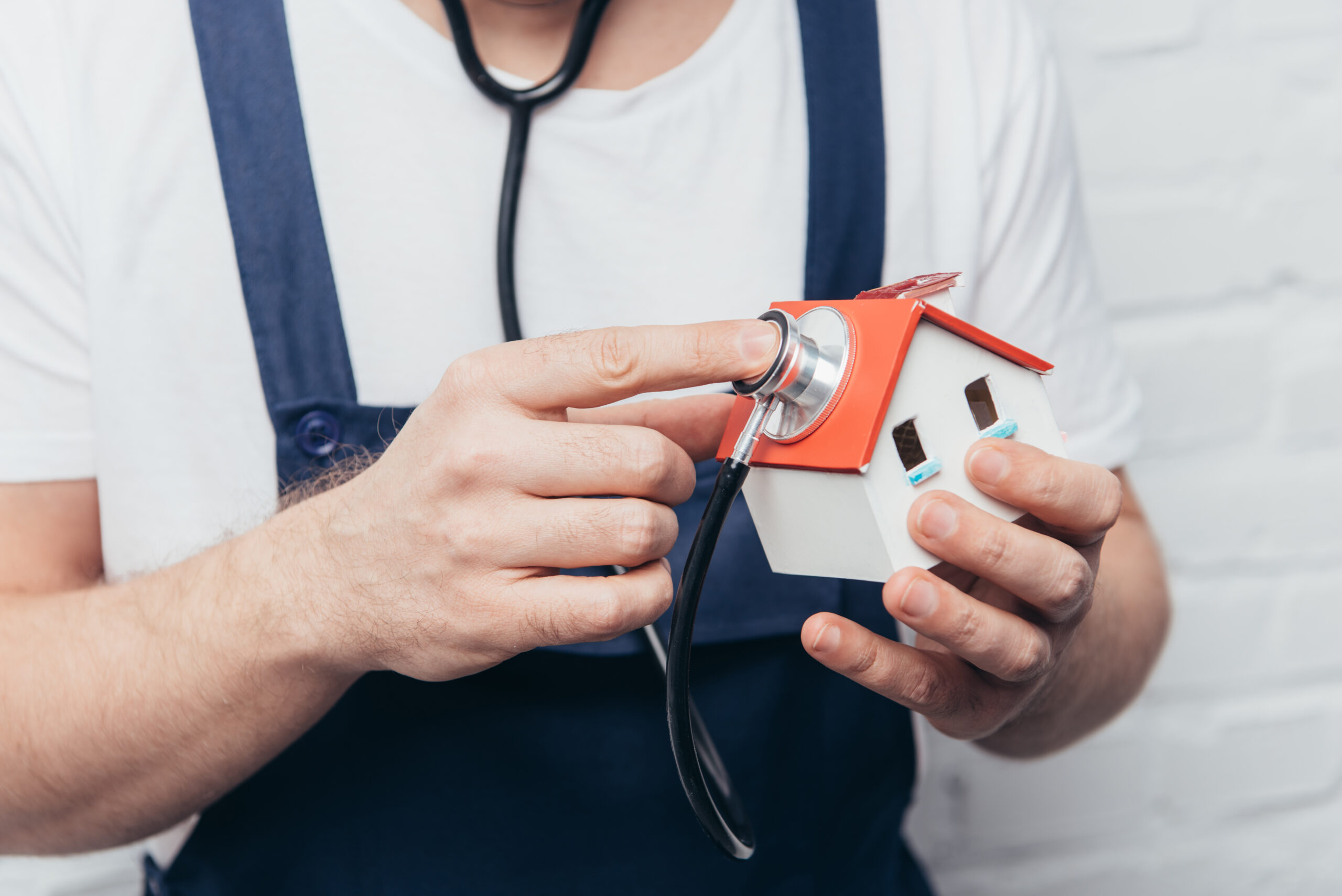 inspector holding stethoscope to handheld model of house