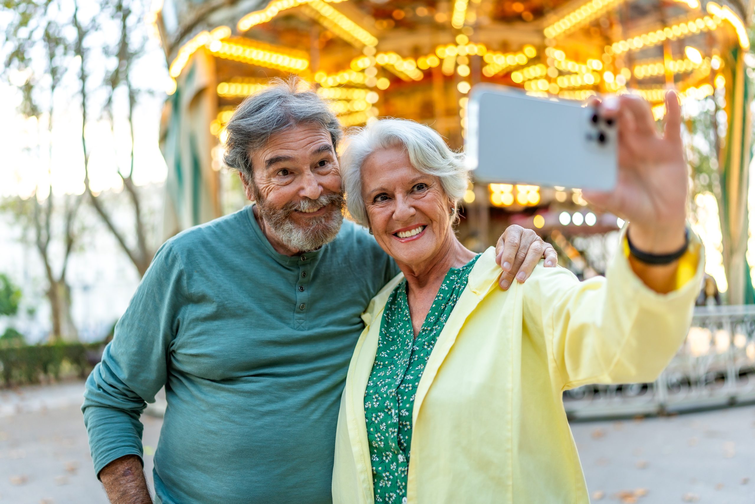 senior couple taking selfie in front of carousel